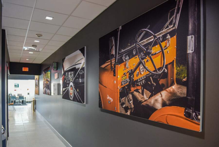 A hallway with vintage car art hung on the walls, featuring sleek flooring and modern lighting. Contact us for more info!